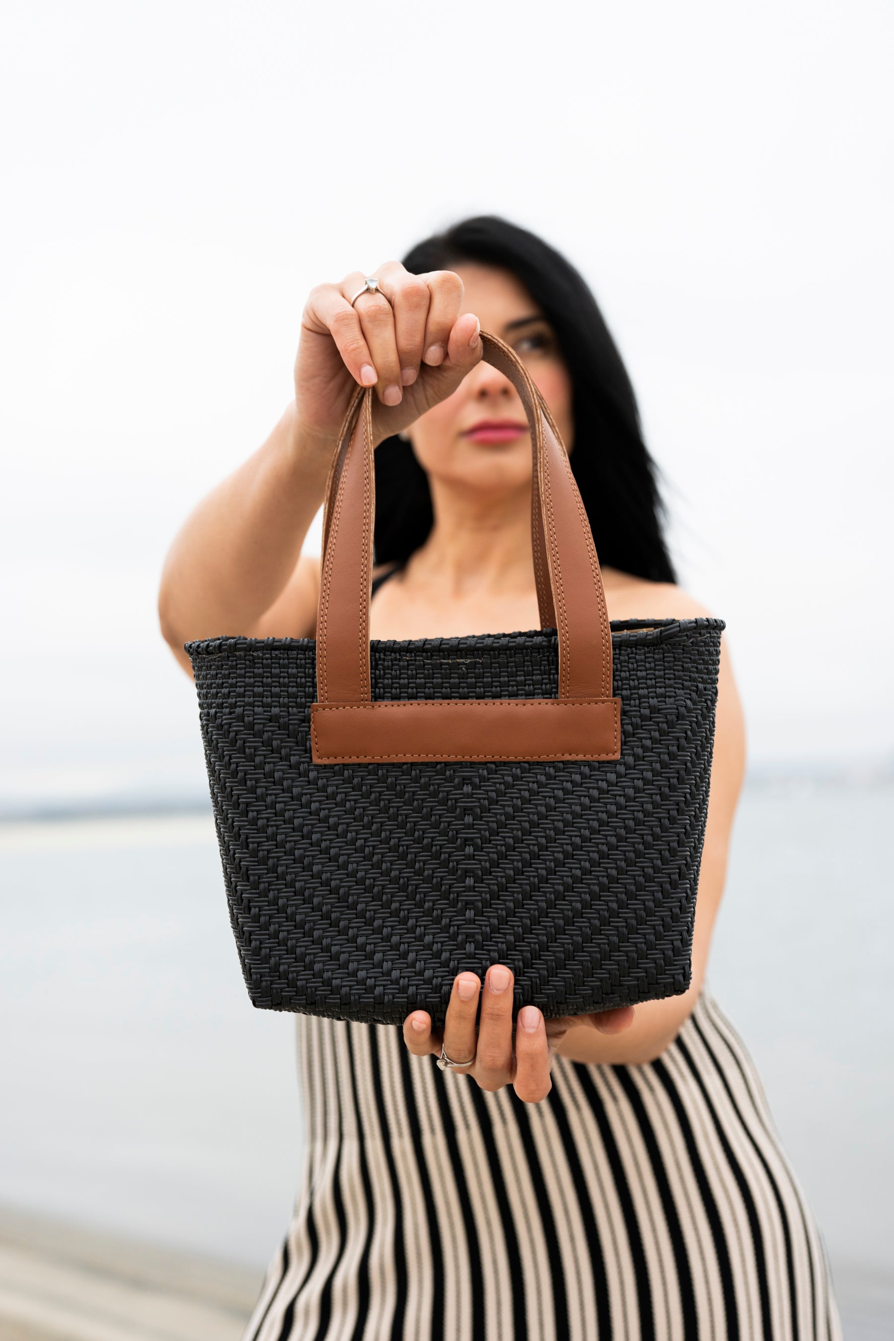 Elegant women holding a Mavis by Herrera Mini tote bag in black woven texture with leather brown handles