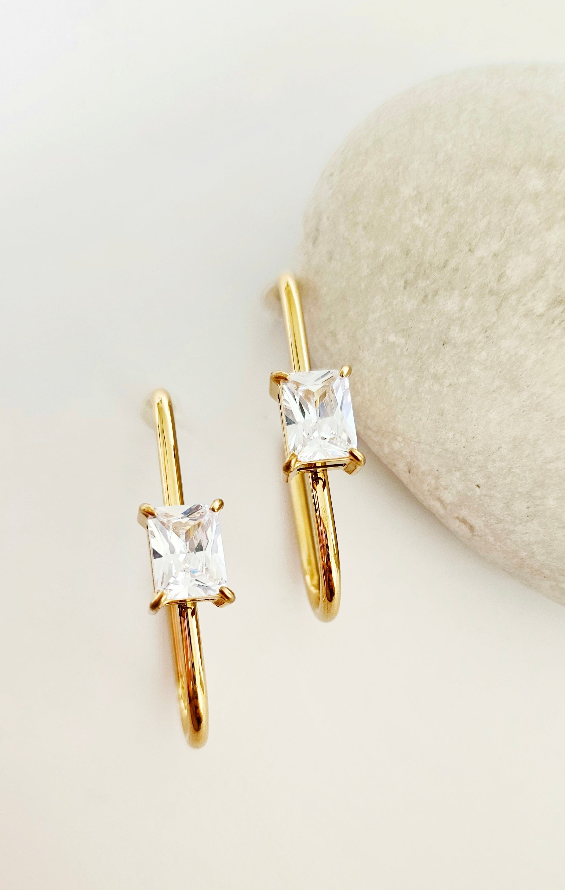 Gold stud earrings with clear gemstones on a light background