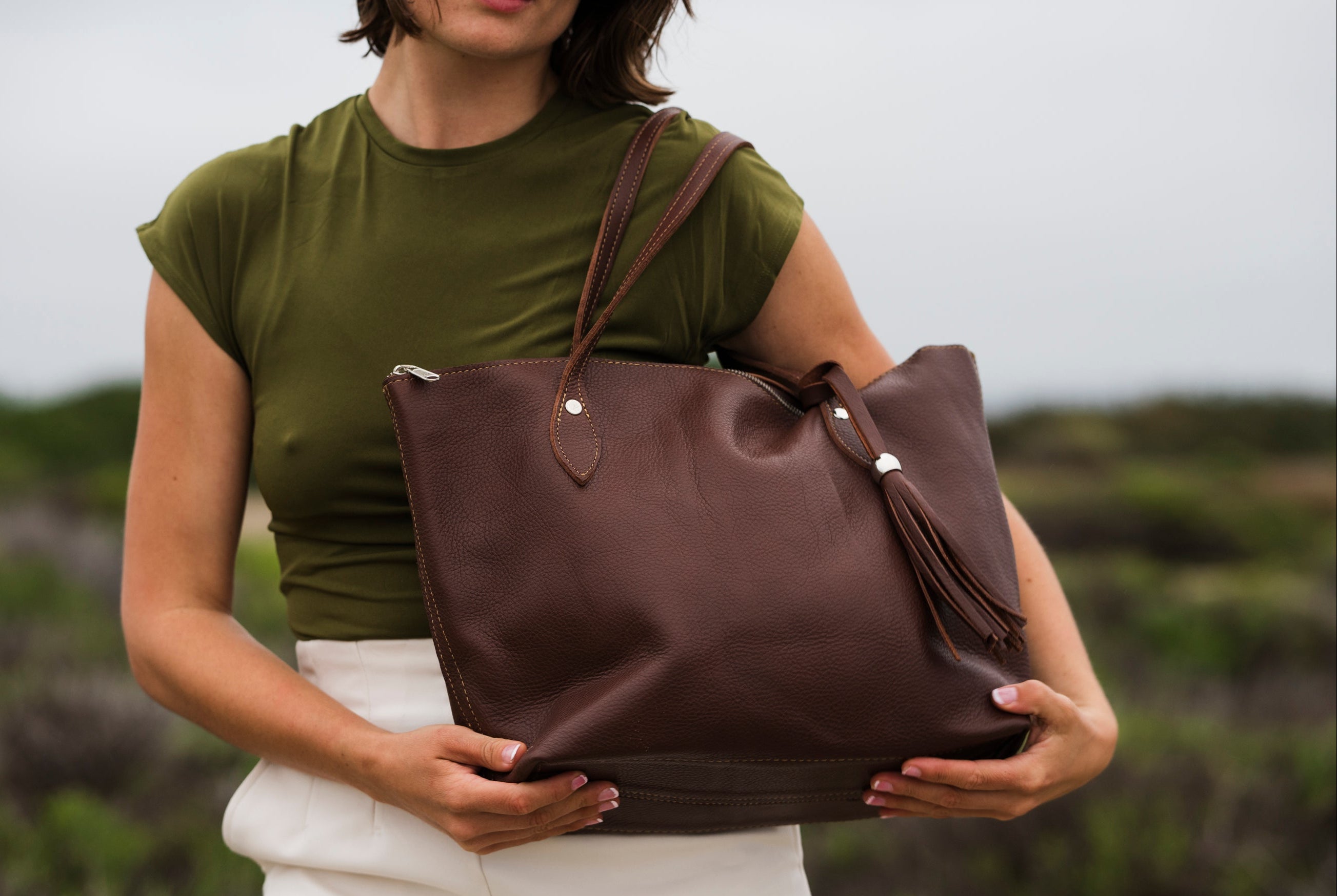 Woman holding a brown leather tote bag in an outdoor setting
