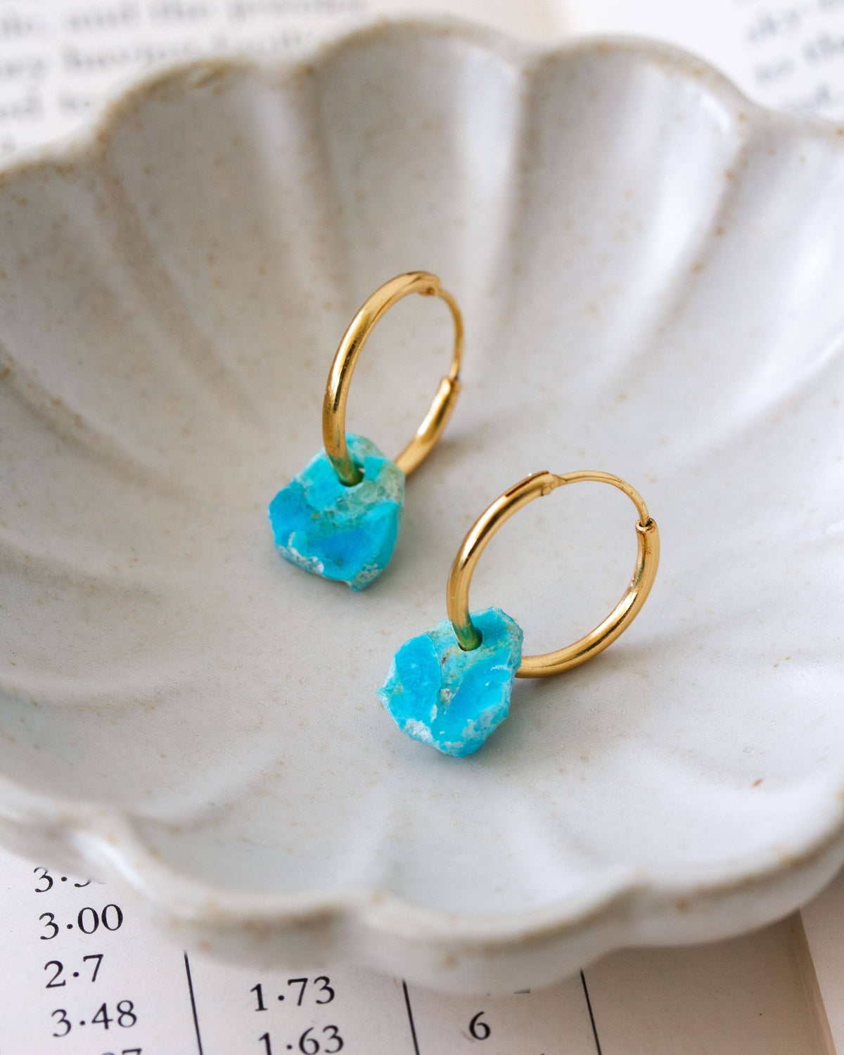 Turquoise Serenity Mini Hoop Earrings: gold-tone mini hoop earrings with turquoise stone drops on a shell.