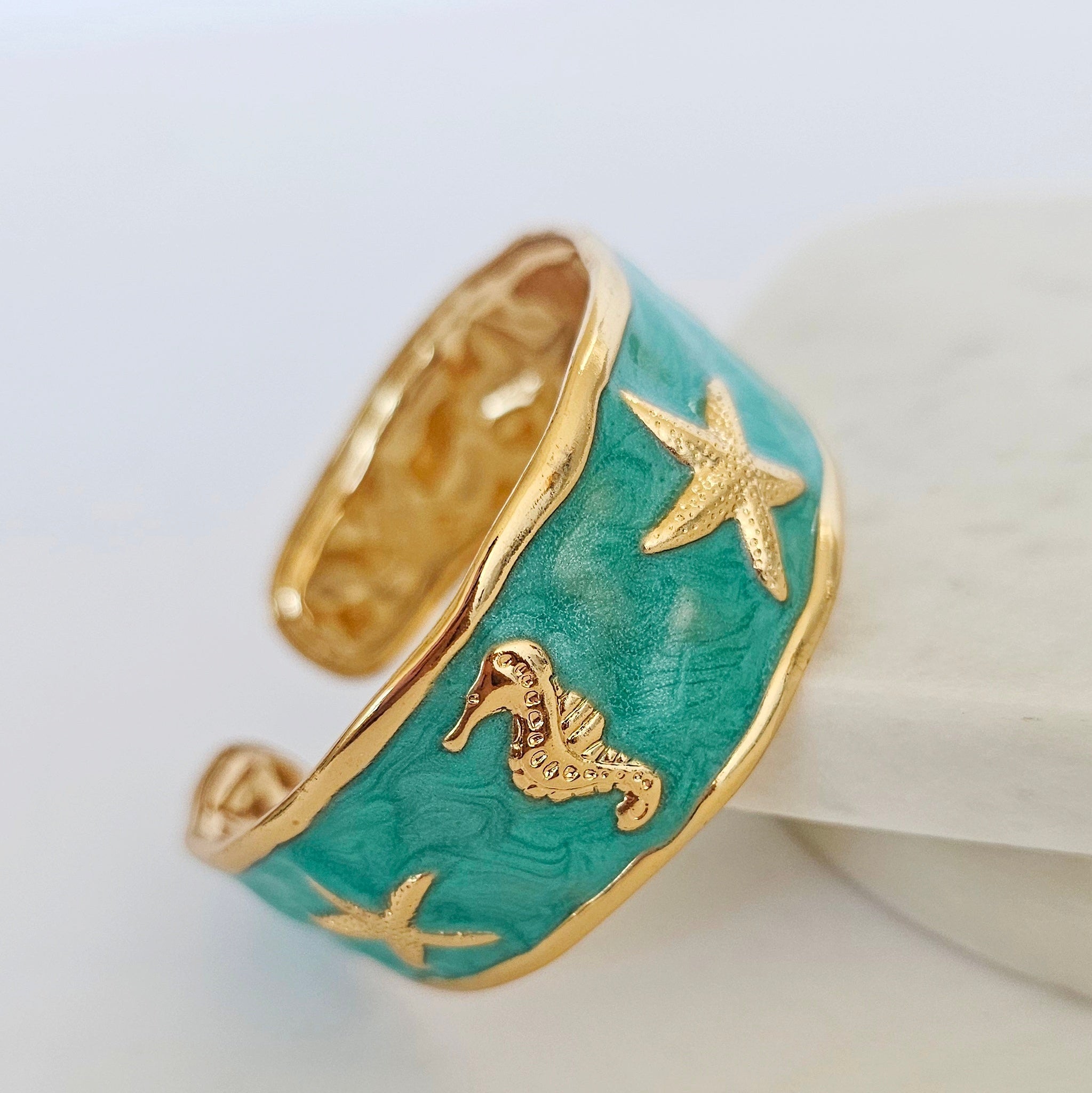 Turquoise ring with gold accents featuring starfish and a seahorse design on a white background