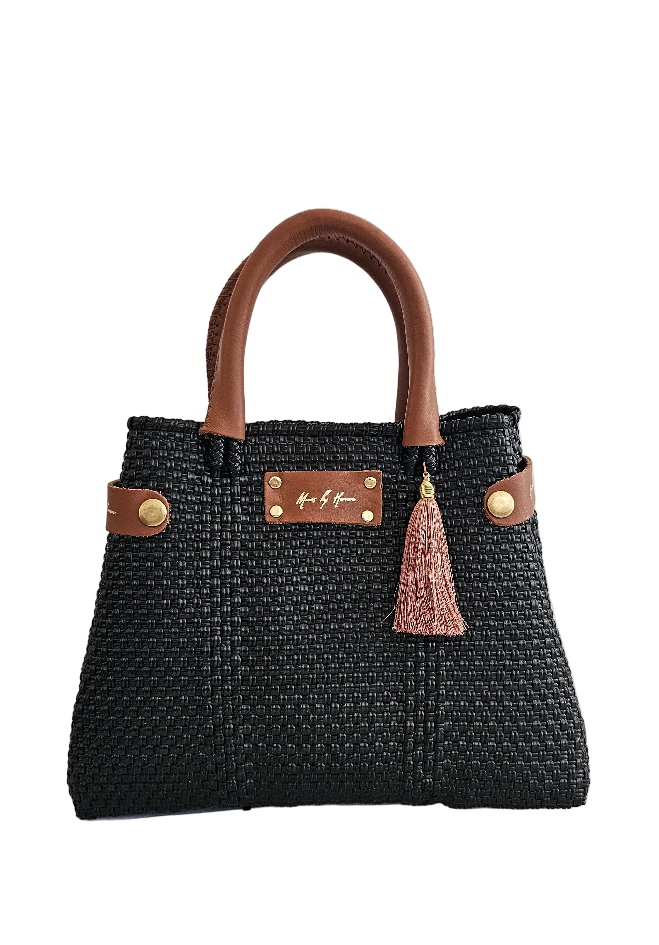 A black woven straw handbag with brown leather handles and trim, featuring a brown tassel charm
