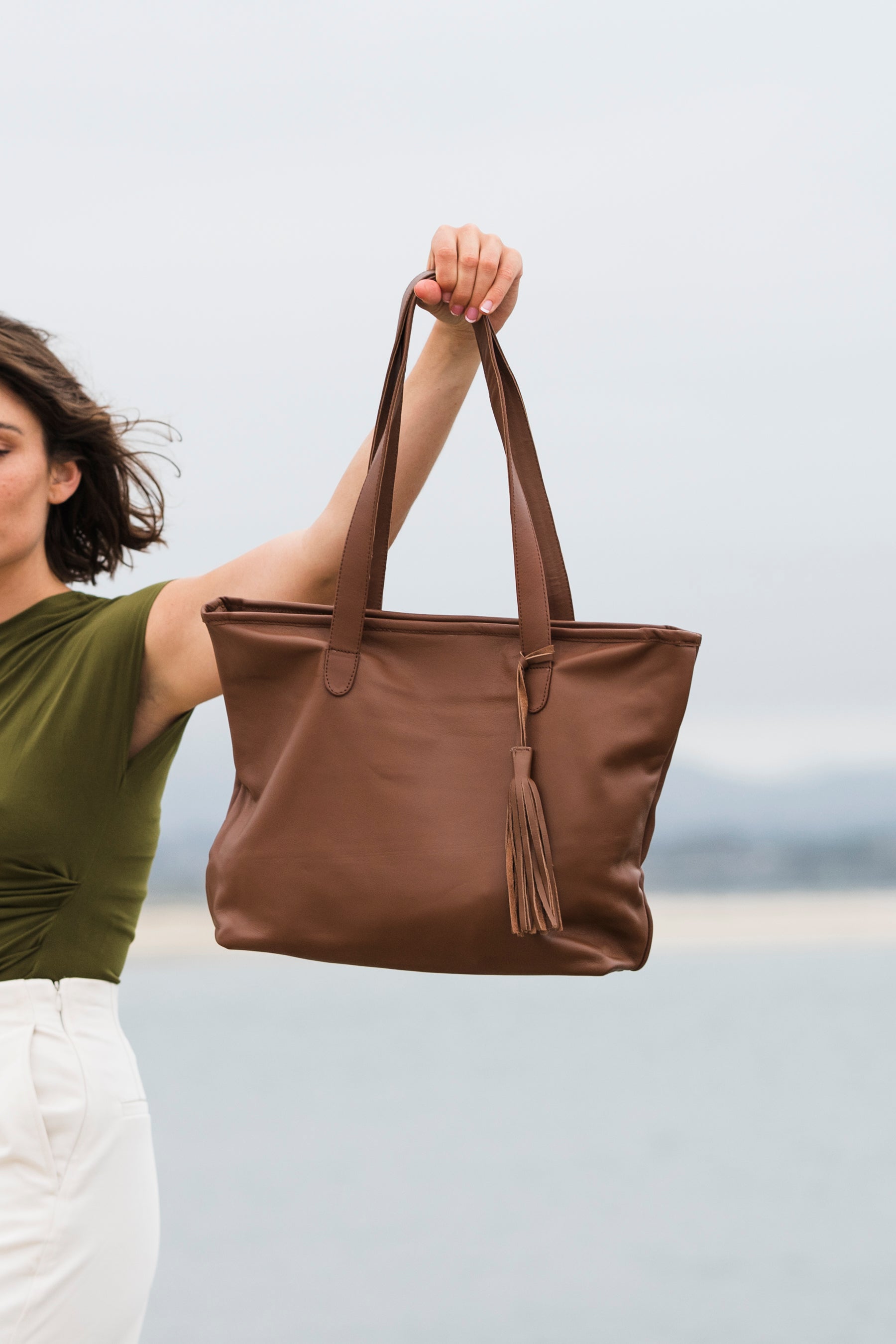 Woman holding a brown leather tote bag with a blurred background