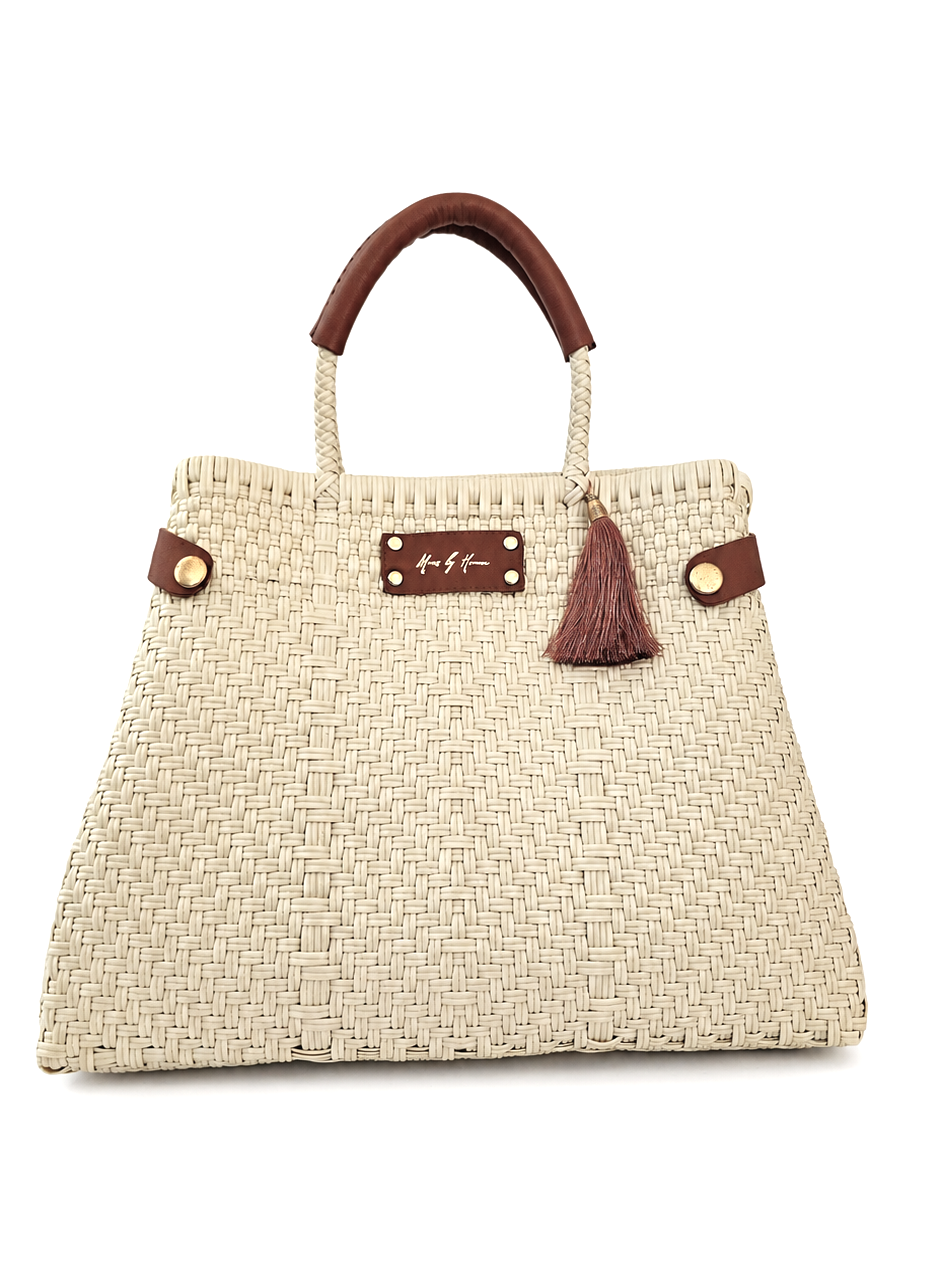 A woven straw handbag in a natural beige color with dark brown leather top handles, a matching leather top handle strap, a tassel charm, and gold-tone hardware.
