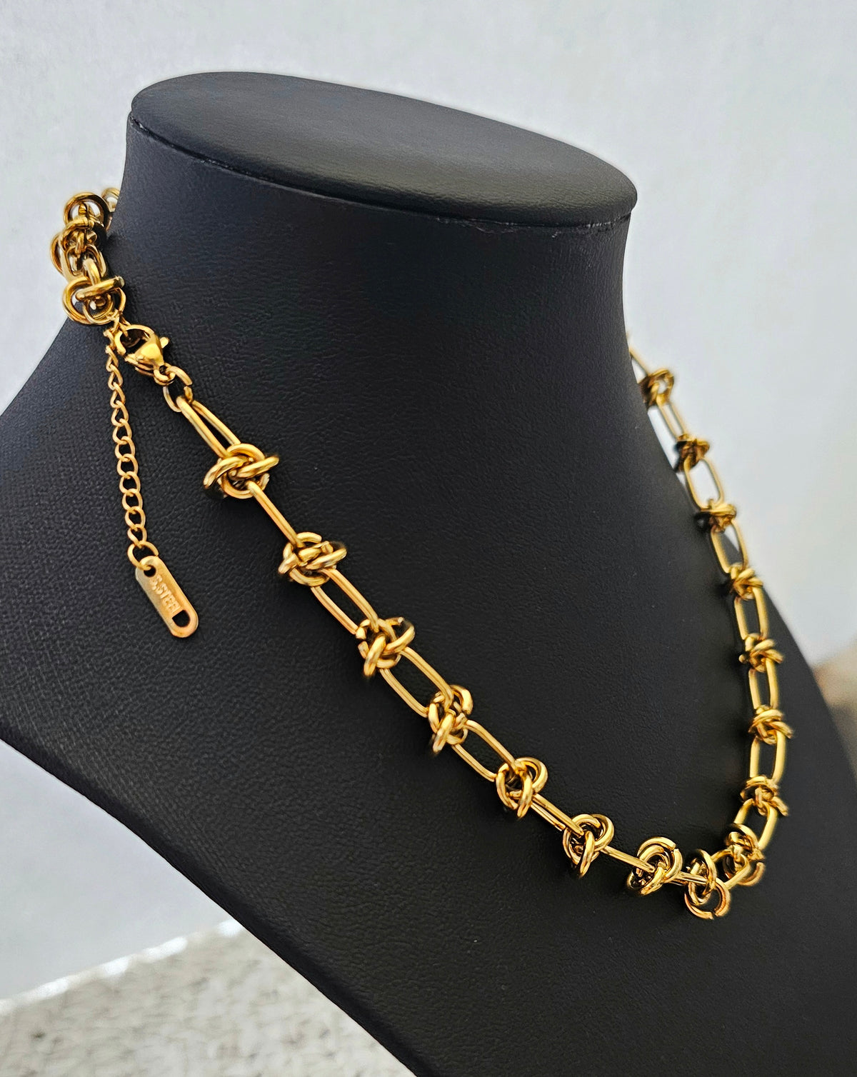 Luxe Knot Necklace: gold-tone knot-link necklace on a black display bust.