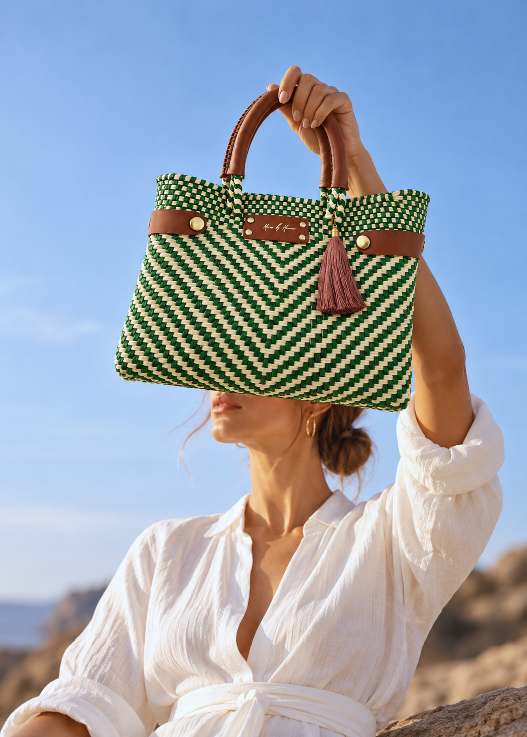 Female model in a white linen outfit holding the Mini Less Pollution Convertible Crossbody & Tote Bag in Palm Verde by Mavis by Herrera, featuring green and ivory handwoven detailing, cognac leather handles, and a tassel.