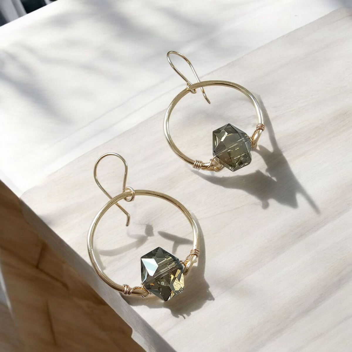 The Crystalline Earrings: hoop earrings with faceted crystal pendants, angled view.